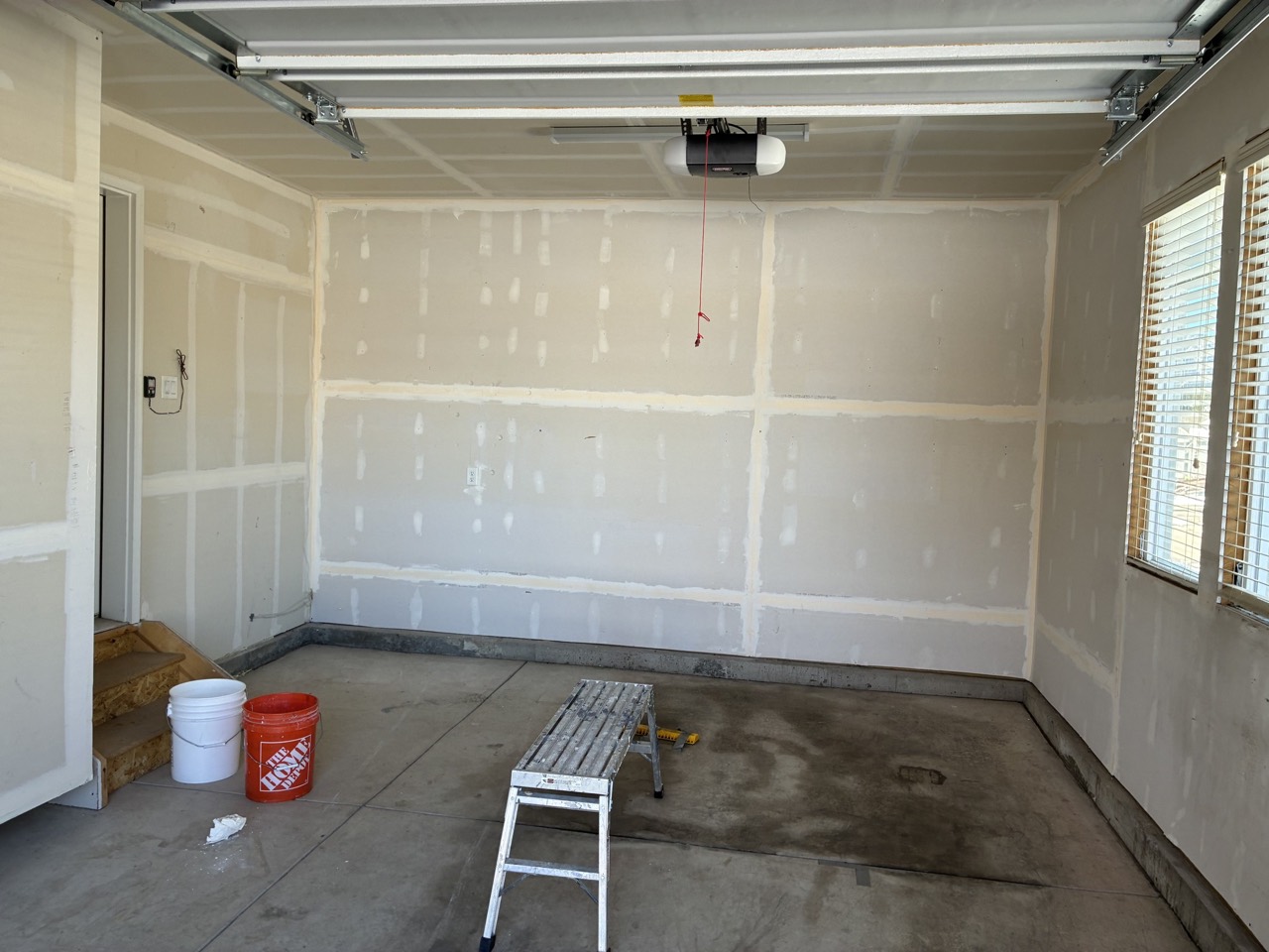 Garage during drywall finishing, wide view of mudded wall and ceiling seams over bare concrete